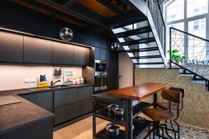 A modern kitchen with dark cabinetry, a built-in oven, and a dining area with a wooden table and chairs. - Luxury Family Home 3BR / 3BA 200m² Duplex | A/C | Walkable area | (Budapest)