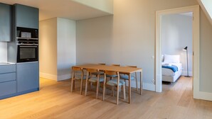 A modern kitchen with built-in appliances, a dining area with a wooden table and chairs, and a bedroom with a bed and bedside lamp. - FLH Heart of Rossio Apartment II (Lisboa ciudad)