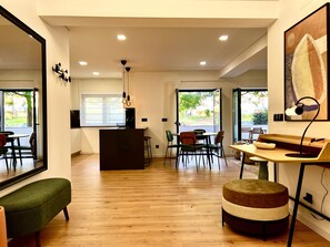 Ein modernes Wohnzimmer mit Holzboden, einem grünen Sofa, einem Holzesstisch mit Stühlen und einer Küchenzeile mit schwarzer Arbeitsplatte und einem Fernseher.