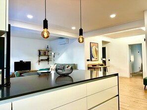 A modern kitchen with a central island, pendant lights, and a dining area with a sofa and table. - FLH Classy & Modern apartment in Cascais (Cascais)