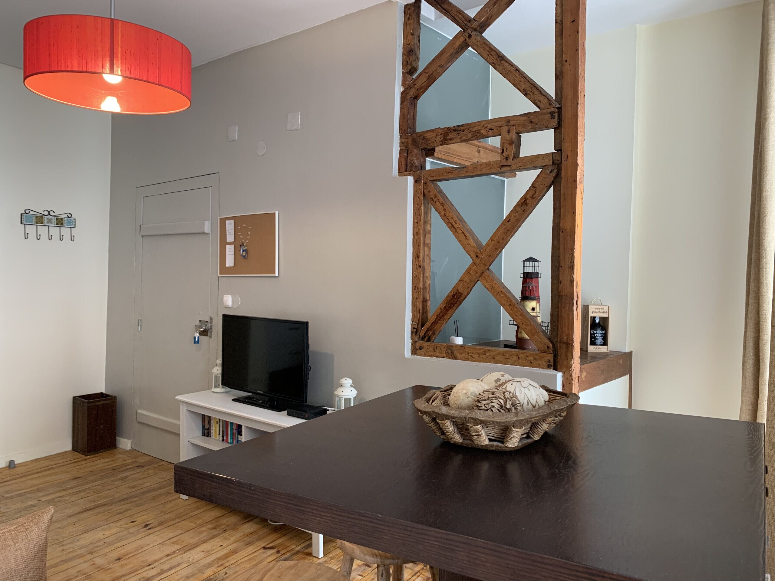 Ein modernes Wohnzimmer mit einem dunklen Holztisch, einer roten Pendelleuchte, einem Fernseher und einem dekorativen Korb.