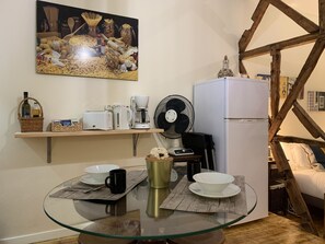 Eine kleine Küche mit einem Glastisch, weißen Geräten und einem Ventilator.