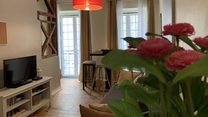 A living room with a television, a red pendant light, a wooden beam structure, a dining area with a table and chairs, and a large window with curtains. - FLH Bairro Alto Central Flat with Pateo (Lisboa ciudad)