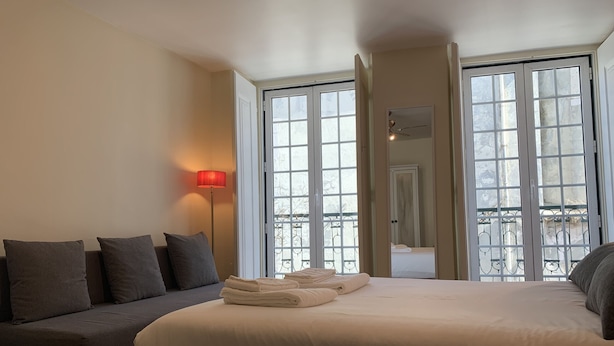 Une chambre avec un grand lit, un canapé et une lampe sur pied. De grandes fenêtres offrent une vue sur l’extérieur.
