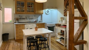 Une cuisine compacte avec des meubles en bois, un lave-linge encastré, une cuisinière et un petit coin repas avec des tabourets.