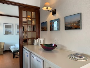 A kitchen with a white countertop, a coffee maker, a bowl, and a sink. There are framed pictures on the wall and a window with a view of a landscape. - FLH Cascais Charming Old Town (Cascais)