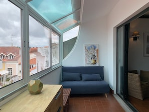 A modern room with a large window, a blue sofa, a wooden table, and a painting on the wall. - FLH Cascais Charming Old Town (Cascais)
