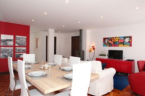 Ein moderner Essbereich mit einem Holztisch, gedeckt für sechs Personen, weißen Stühlen und einer roten Wand mit Schwarz-Weiß-Fotos.