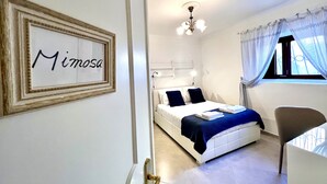 A bedroom with a bed, a chair, a bedside table, a ceiling light, a window with curtains, and a framed sign on the wall. - FLH Yucca House Carcavelos Beach (Cascais)