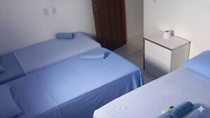 A room with two single beds, each with a blue bedspread and pillows. There is a small white table with a roll of toilet paper on it. - Pousada Delta (São Luís)