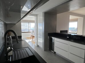 Eine moderne Küche mit schwarzem Arbeitsplatz, weißen Schränken und Blick auf die Stadt durch große Fenster.
