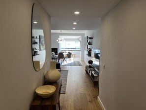 Ein modernes Interieur mit Holzboden, einer Essecke mit Stühlen und Tisch sowie einer Küche mit Fernseher und Regalen.