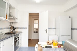 Eine moderne Küche mit weißen Schränken, einem Edelstahlkühlschrank und einem Essbereich mit Tisch für zwei Personen.