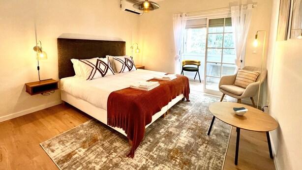 Habitación de hotel con una cama grande, una mesita pequeña, una silla y vistas al exterior.