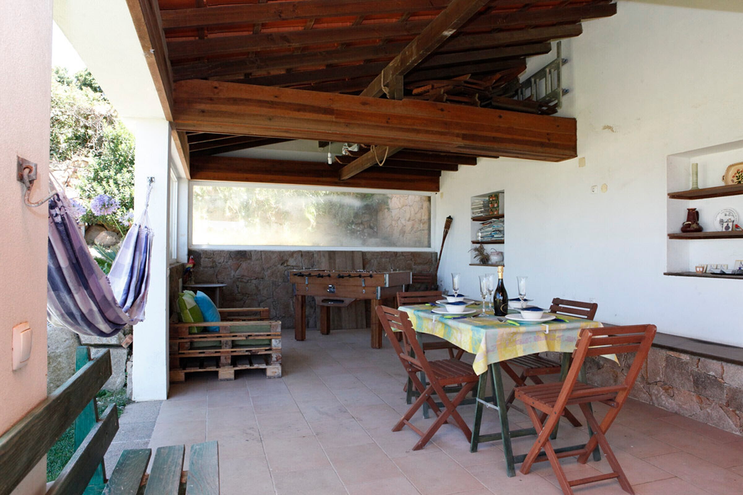 An outdoor patio with wooden furniture, a table set for dining, and a hammock.