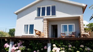 Una casa de dos pisos con balcón, ventanas grandes y fachada de piedra.