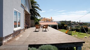 Una terraza de madera con dos sillas de mimbre, una mesita y un área de juegos infantiles con un tobogán.
