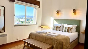 Ein Schlafzimmer mit einem großen Bett, einer Bank, einem Fenster mit Aussicht und zwei Wandleuchten.