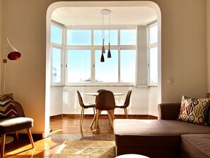 A modern living room with a dining area, large windows, and a view of the city. - FLH Cascais Apartment with Incredible View (Cascais)