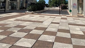 Una amplia plaza pública con pavimento a cuadros, rodeada de edificios de varios pisos con balcones y comercios, incluyendo un restaurante.