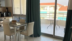 Cocina moderna con comedor, ventanas amplias y vista a un edificio y una piscina.