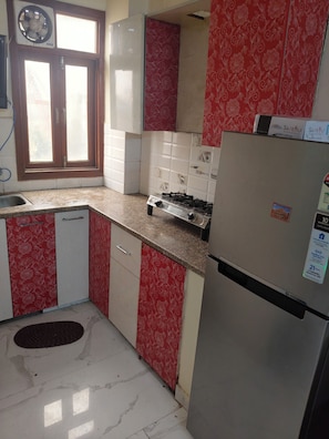 Una cocina con armarios de estilo rojo y blanco, un refrigerador de acero inoxidable, una estufa a gas y una ventana con persianas.