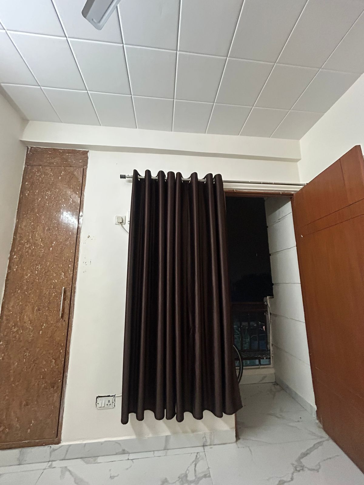 A room with a tiled ceiling, a brown door, a curtain, and a tiled floor.