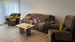 Ein modernes Wohnzimmer mit einem braunen Sofa, zwei Sesseln, einem Holztisch und einer karierten Decke.