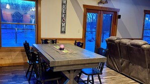 Un comedor con una mesa y sillas de madera, un letrero con la palabra 'WELCOME' y amplias ventanas que ofrecen vistas al exterior.