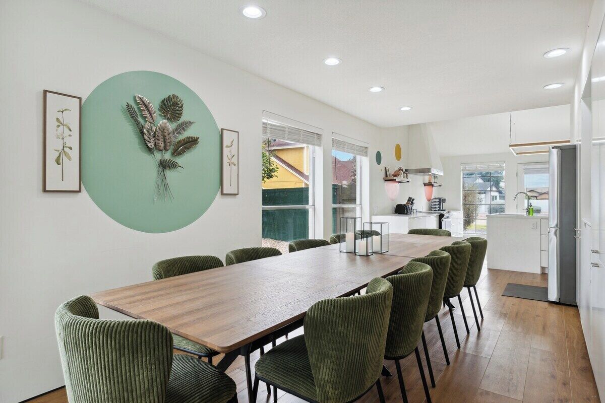 Una cocina moderna con comedor, que presenta una mesa de madera larga y sillas tapizadas en verde.