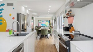 Een moderne keuken met witte kastjes, een houten eettafel en groene stoelen.