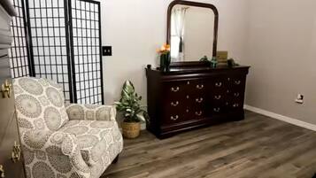 Une pièce avec un fauteuil à motifs, une commode en bois foncé dotée d’un miroir et un plancher en bois.
