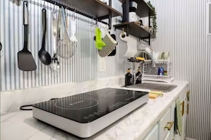 Una cocina con tope de inducción negro, utensilios colgantes y un salpicadero blanco a rayas.