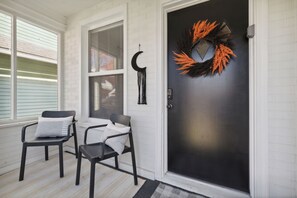 Eine Veranda mit zwei schwarzen Stühlen, einer schwarzen Tür und einem Girlanden-Dekoration.