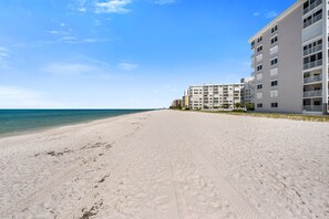 A wide sandy beach with a clear blue sky and ocean. There are multi-story buildings with balconies along the beach. - Heavenly Naples beach front 2 bed 2 bath condo (Naples)