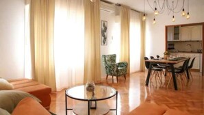 A spacious living area with a round glass table, a sofa, a dining table with chairs, and a kitchen in the background. - Dare Apartment with private pool and garden (Kaštel Sućurac)