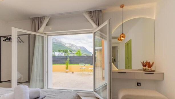 A modern hotel room with a bed, a bench, a mirror, and a view of mountains through large glass doors. - Dare Apartment with private pool and garden (Kaštel Sućurac)
