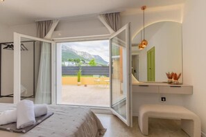 Una habitación de hotel moderna con una cama, un banco, un espejo y vistas a las montañas a través de puertas de vidrio grandes.