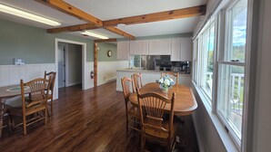 Una cocina amplia con vigas de madera, un comedor con mesa y sillas, y vistas a través de amplios ventanales.