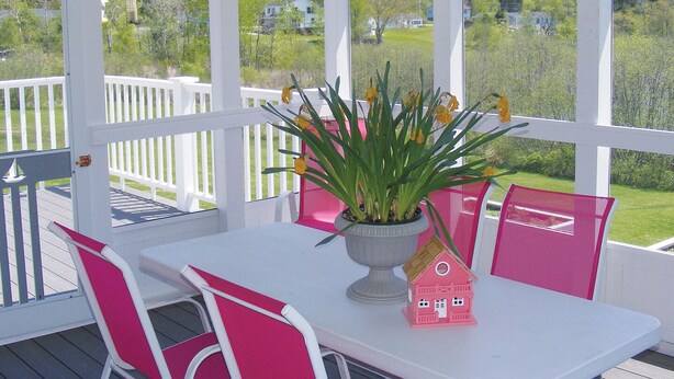 Un espacio al aire libre cubierto con una mesa blanca y sillas rosas, una planta en maceta y un pequeño modelo de casa rosa.