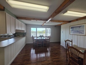 A kitchen with wooden beams, a dining area with chairs, and a view through a window.