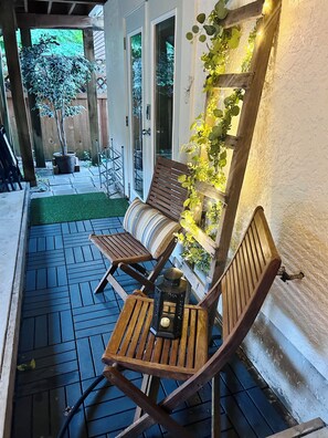 Une terrasse avec des chaises et une table en bois, une petite lanterne et un mur décoré de plantes et de guirlandes lumineuses.