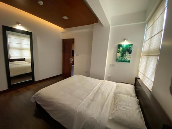 Un dormitorio con cama, espejo, puerta y un cuadro en la pared.
