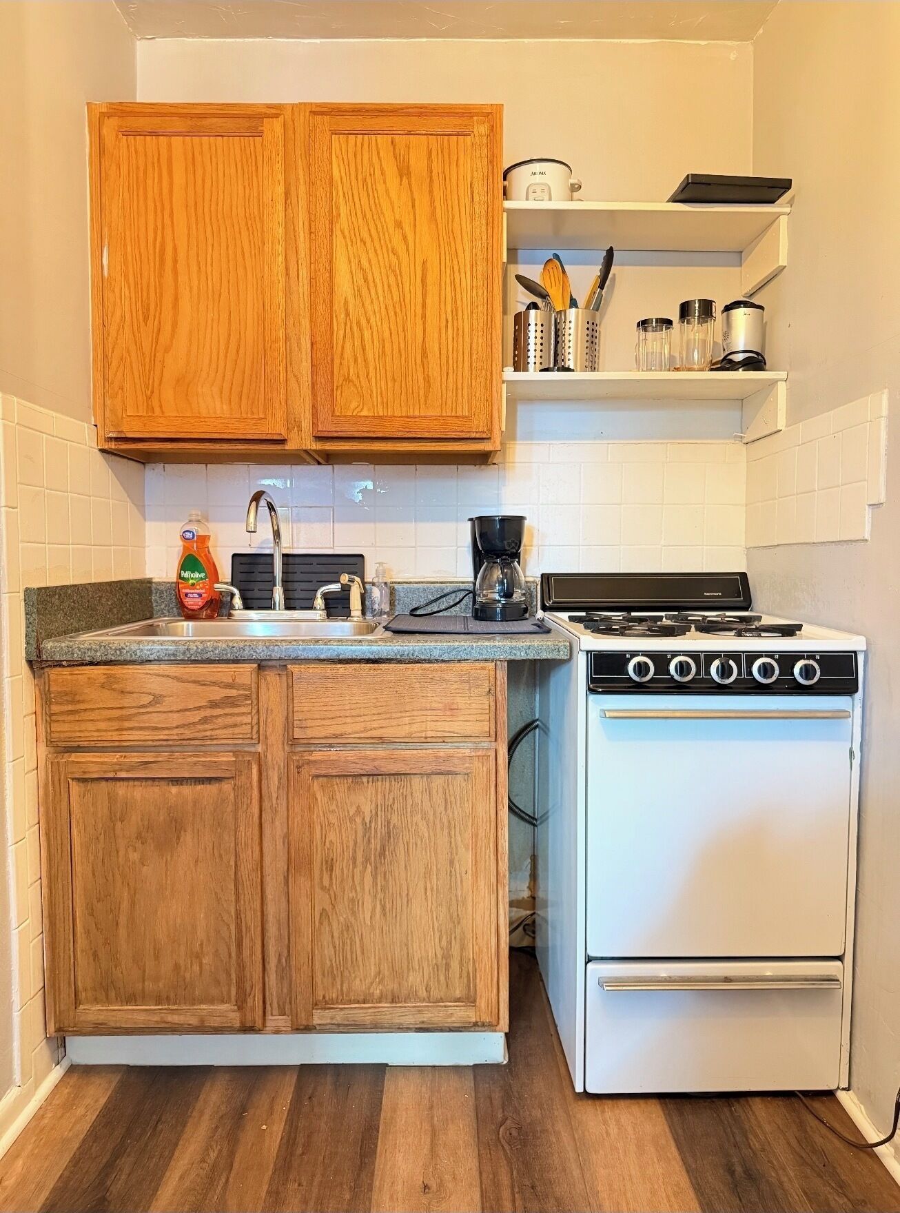 Uma cozinha com armários de madeira, fogão branco, cafeteira e uma prateleira com utensílios de cozinha.
