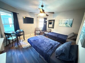 A room with two beds, a desk, chairs, a ceiling fan, and a TV. - Cozy studio in tranquil Rochester with refreshing AC breeze (Rochester)