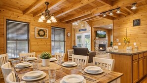 A wooden interior with a dining table set for four, a fireplace, and a kitchen area. - Amazing Grace - Charming Cabin (Sevierville)