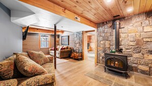 Ein gemütliches Wohnzimmer mit Kamin aus Stein, Holzboden und einer Couch mit gemusterten Kissen.