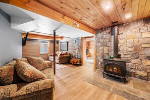 A cozy living room with a stone fireplace, wooden ceiling, and a sofa with patterned cushions. - Stowe Hollow Retreat. Hot Tub, Pet Friendly (Stowe)