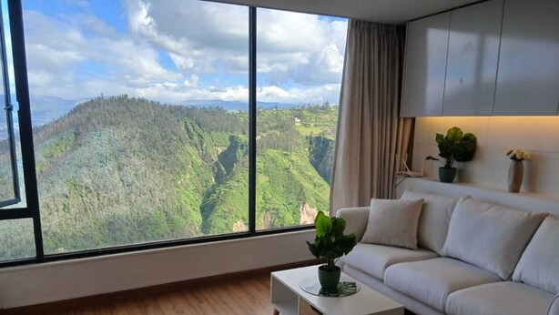 A modern living room with a large window offering a view of a mountainous landscape. - Loft in Quito with the best view and location !!! (Quito)