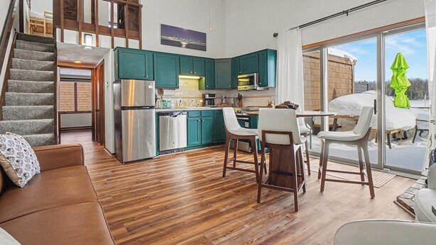 Un'ampia cucina con pavimento in legno, mobili color petrolio e un'area pranzo con sedie bianche.